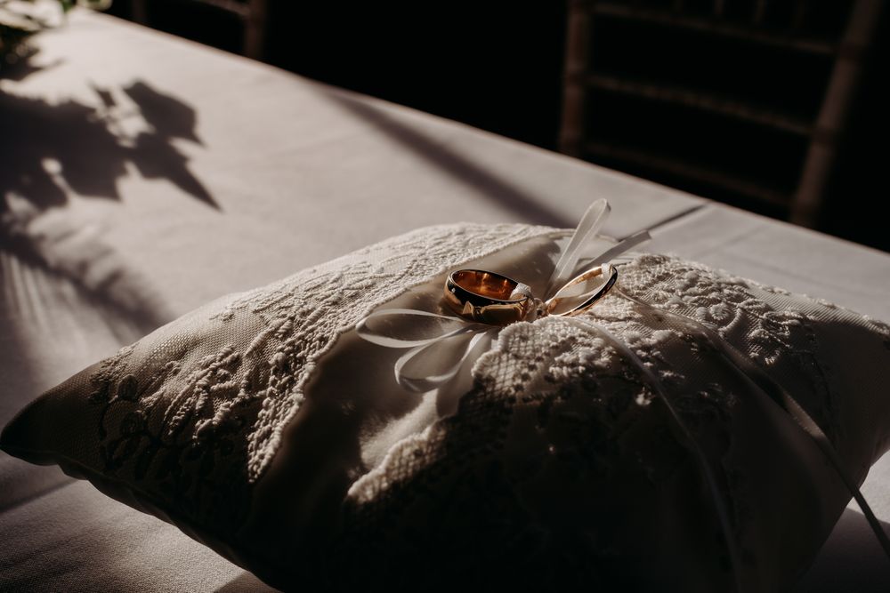 Close-up view of a wedding ring resting on an ornate lace surface with delicate floral embroidery patterns.