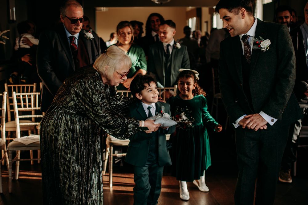 A small child in a navy suit receives a gift from an elderly woman in a sparkly dress at a formal event.