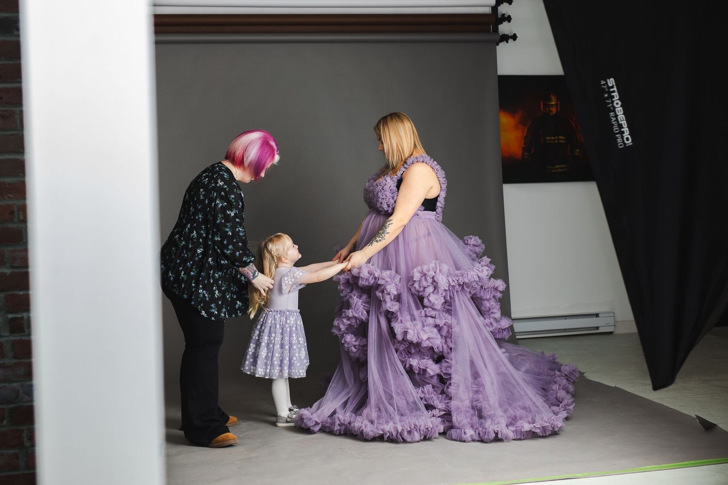 Behind-the-scenes photo shoot of someone in a flowing purple dress being photographed in a studio setting.