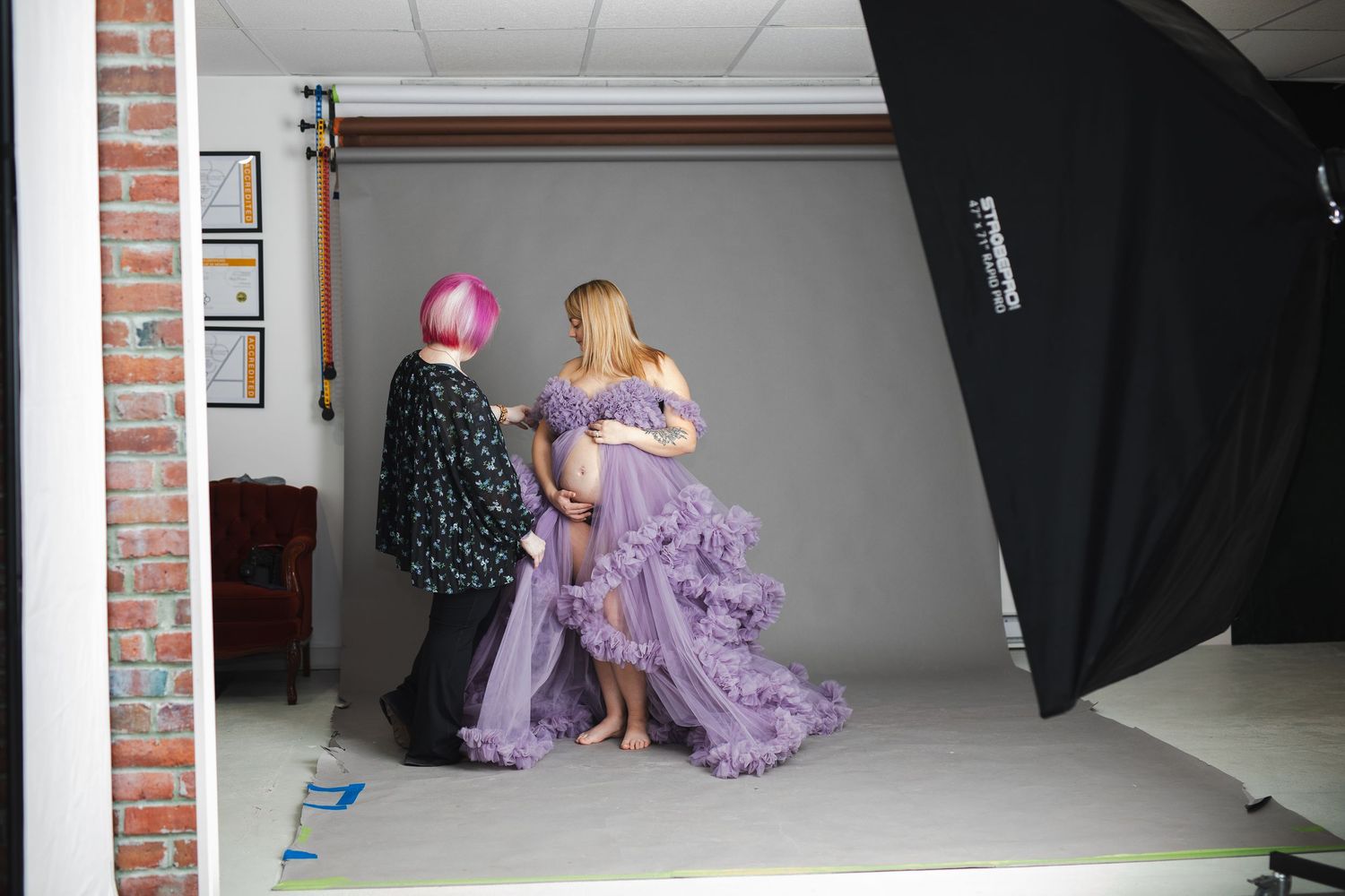 Behind the scenes photo shoot of a model in a flowing purple gown posing against a white backdrop in a studio setting.