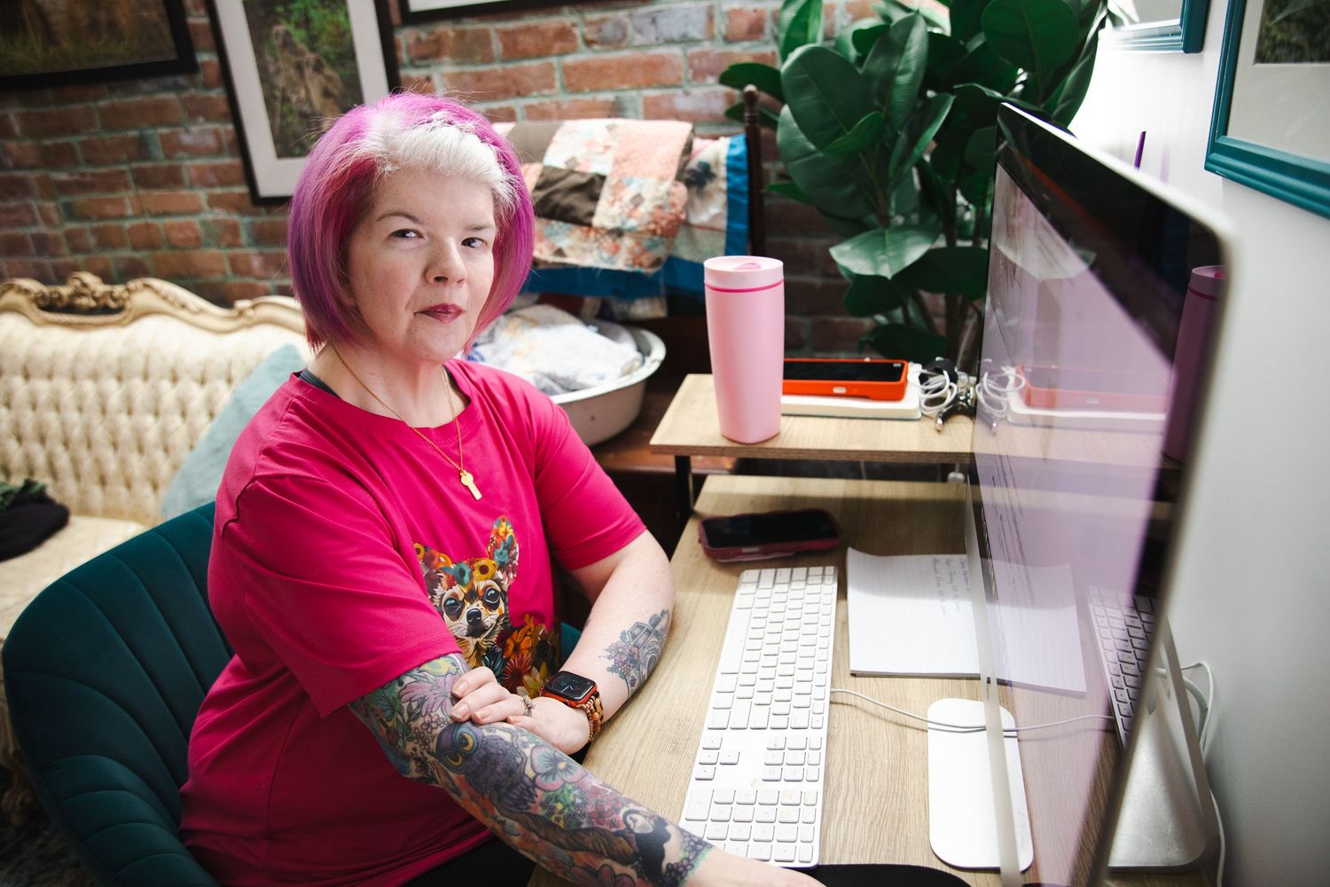 A person sits at a desk with a computer keyboard and monitor in a home office setting with exposed brick walls.