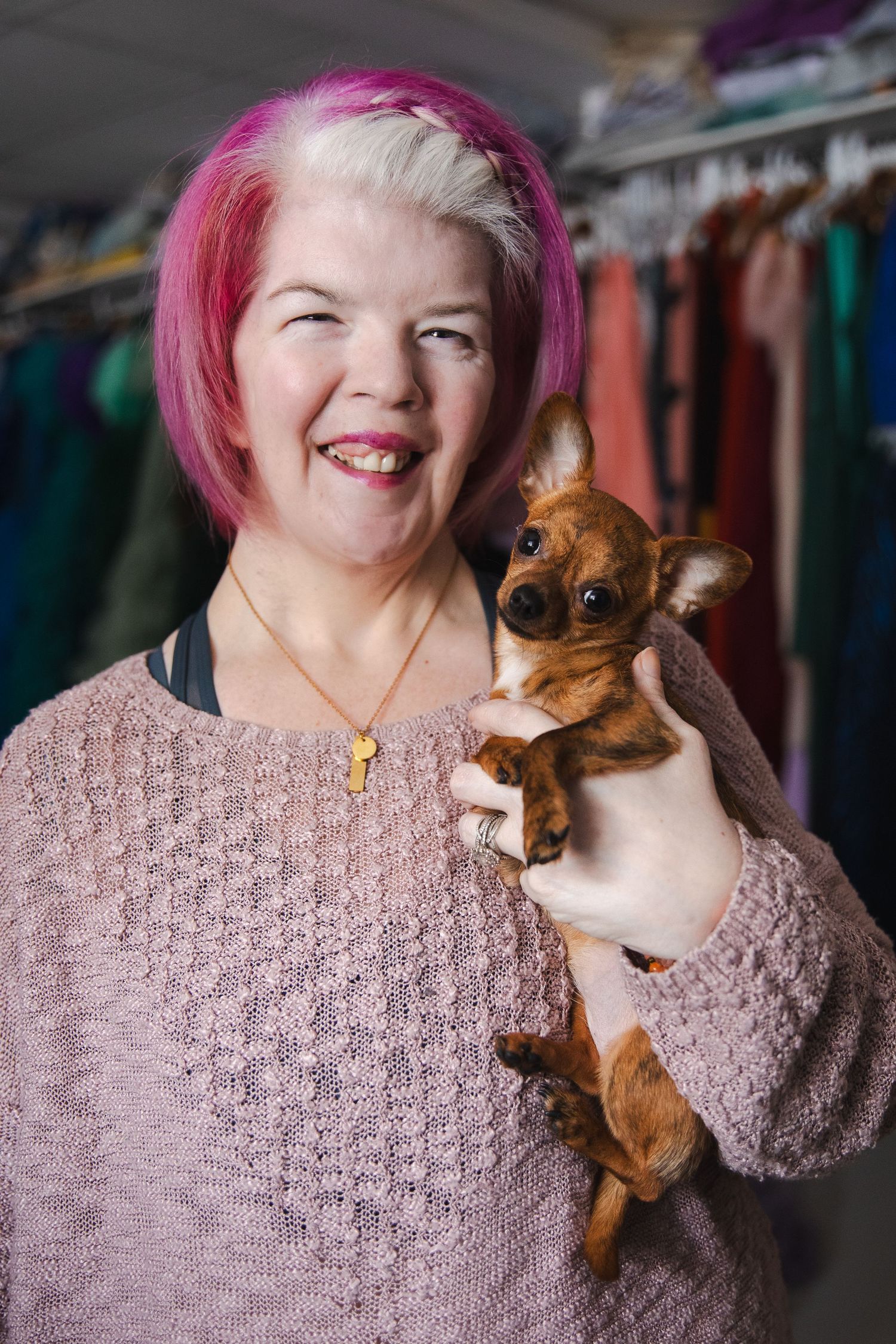 A person with pink hair wearing a knit sweater holds and plays with a small brown dachshund dog in a photo series.