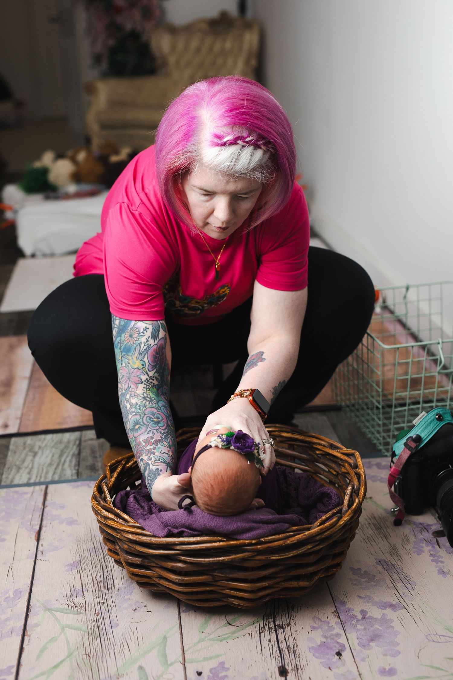 A person in a pink shirt performs yoga stretches while sitting in a woven basket on a wooden floor.