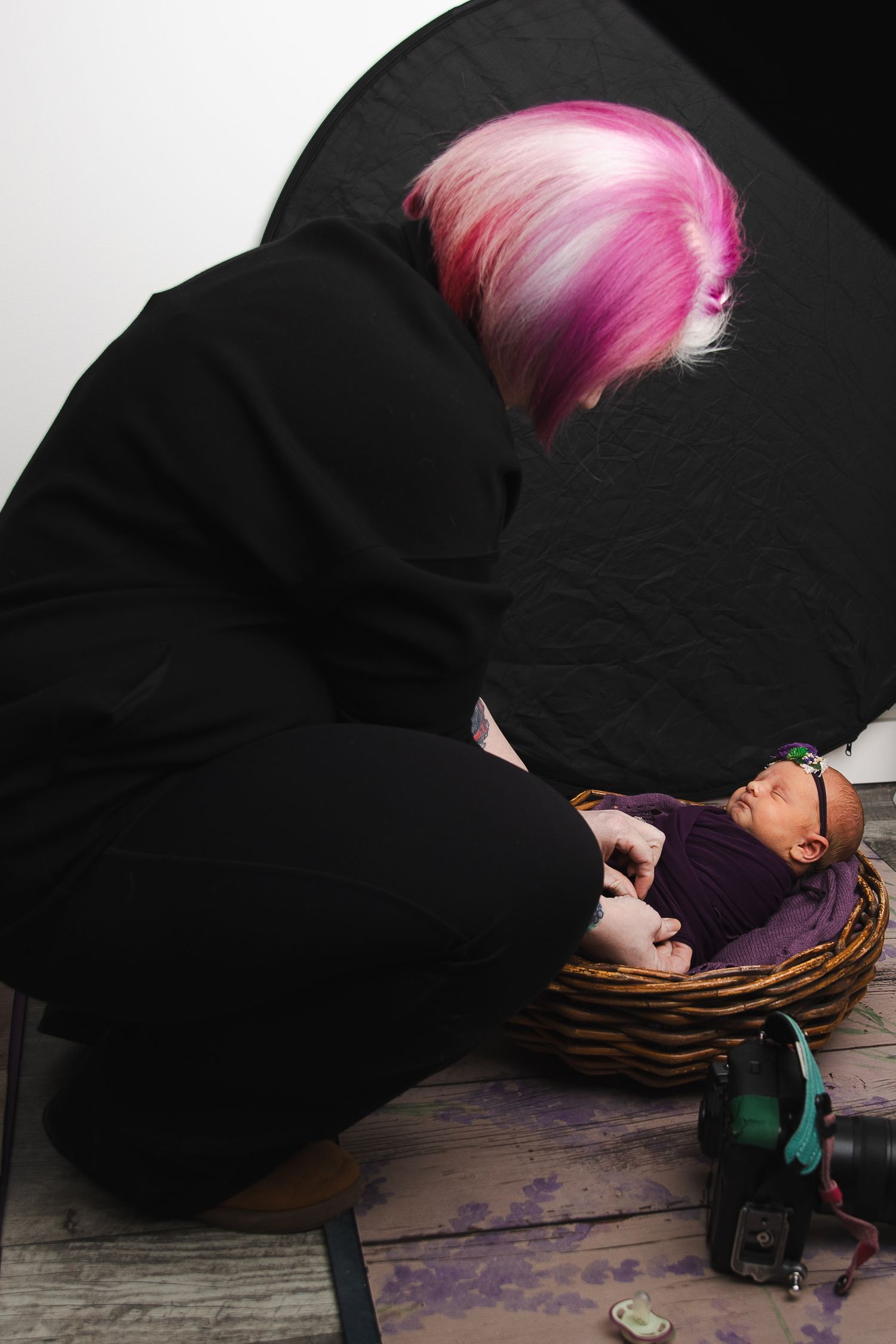 Person with pink hair wearing black lying on wooden floor with dramatic lighting.