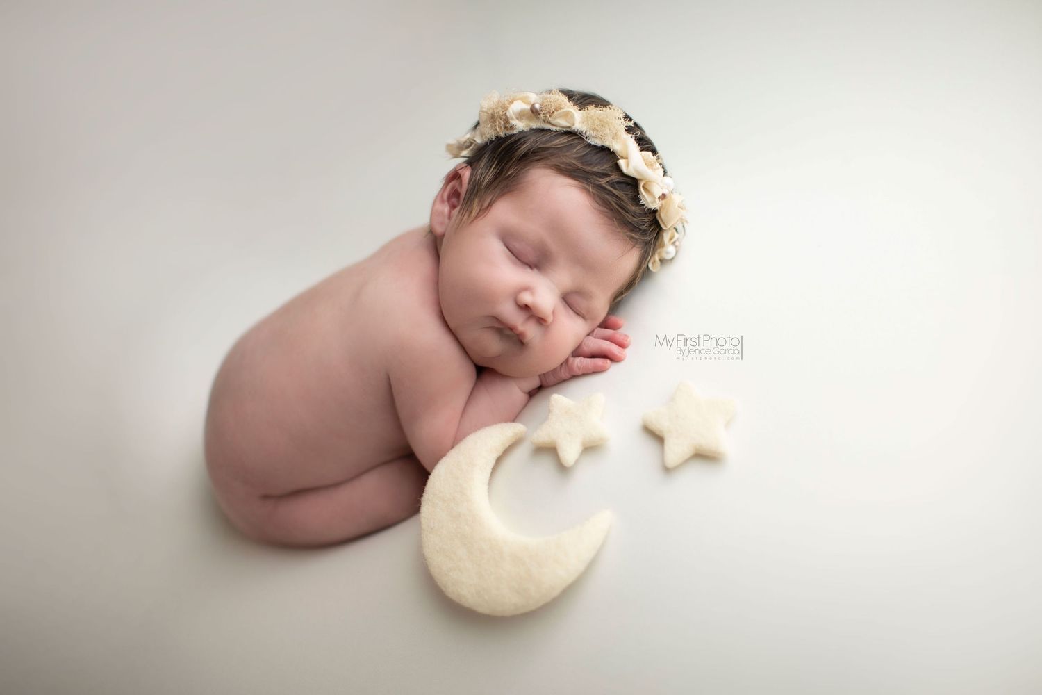 A sleeping newborn baby lies peacefully on soft white fabric with a small white cushion nearby.