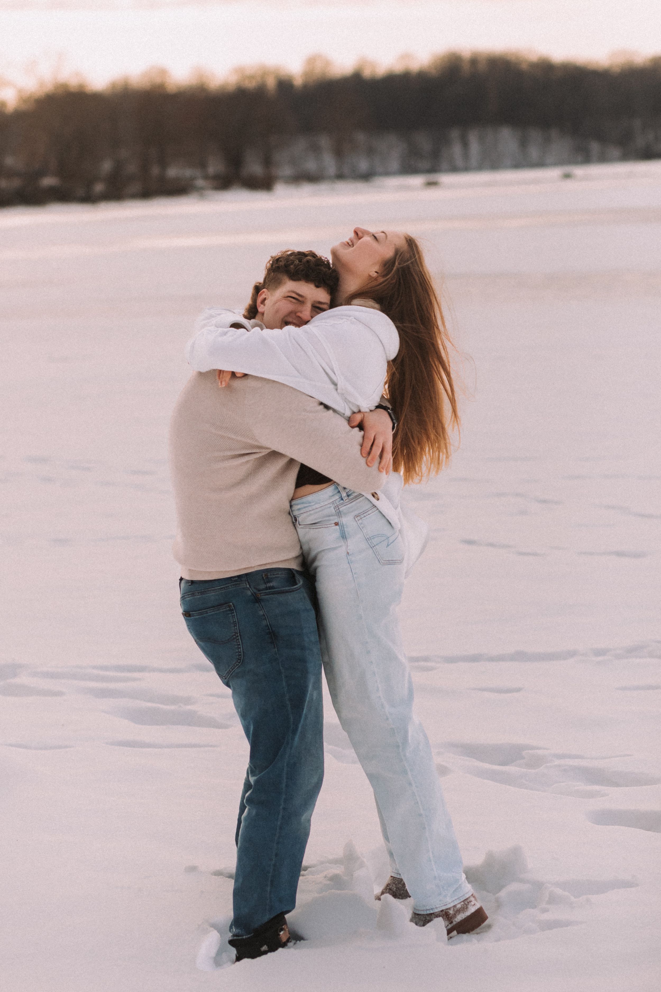 Two people embrace in a romantic moment on a snow-covered landscape during winter.