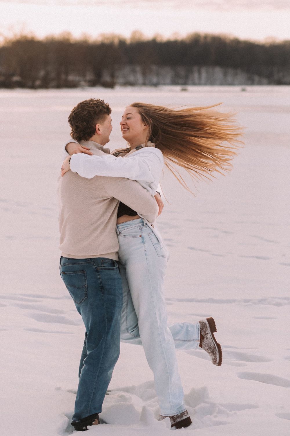 A couple embraces and spins joyfully in the snow during a romantic winter photoshoot.