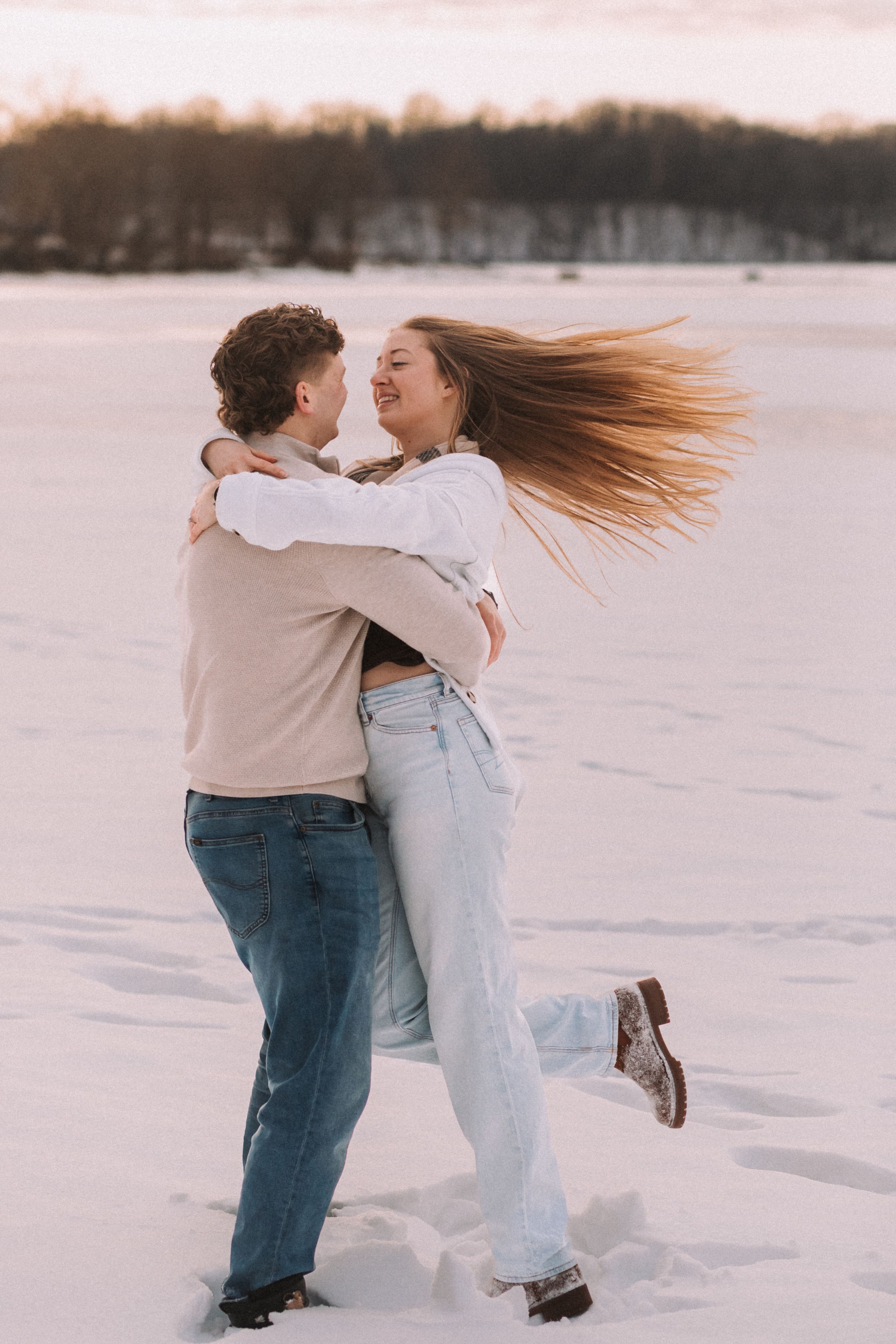 A couple embraces and spins joyfully in the snow during a romantic winter photoshoot.