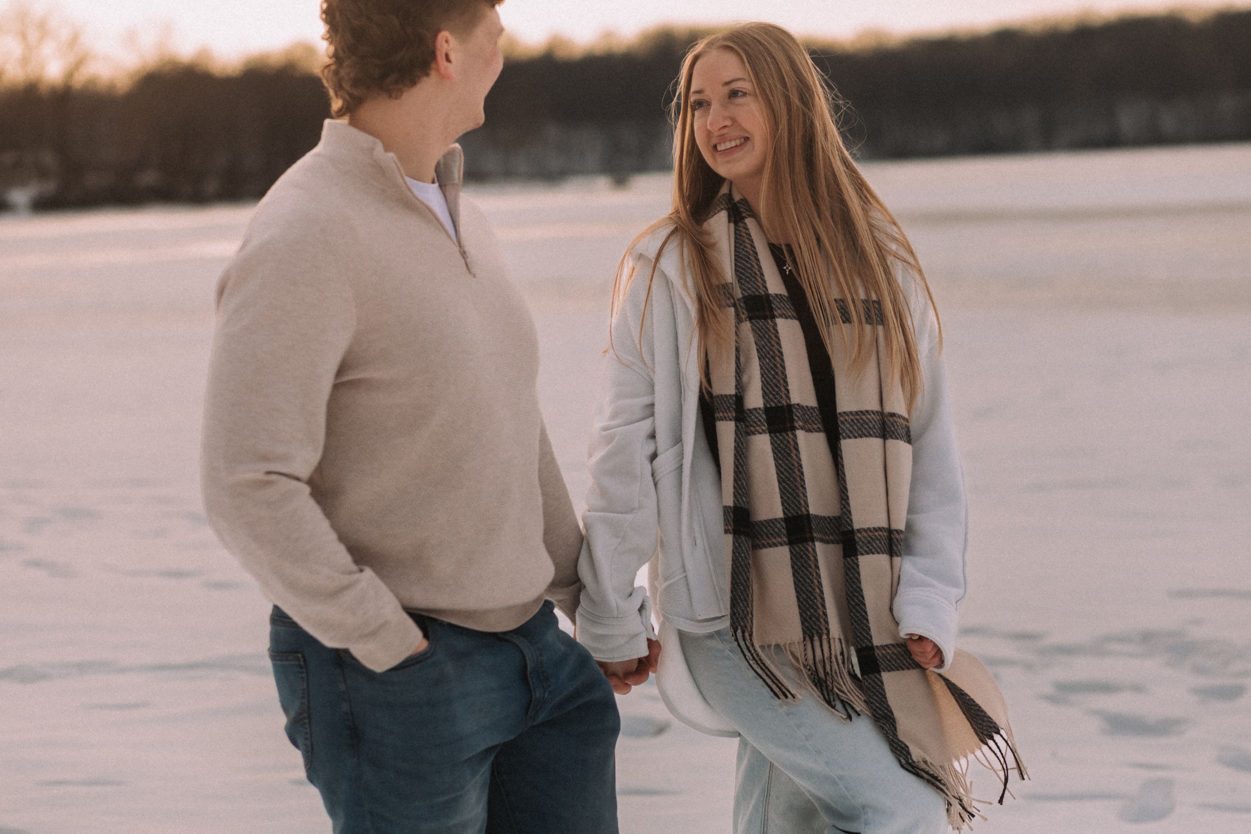 A couple shares a romantic moment on a frozen lake during sunset with snow covered landscape in the background.