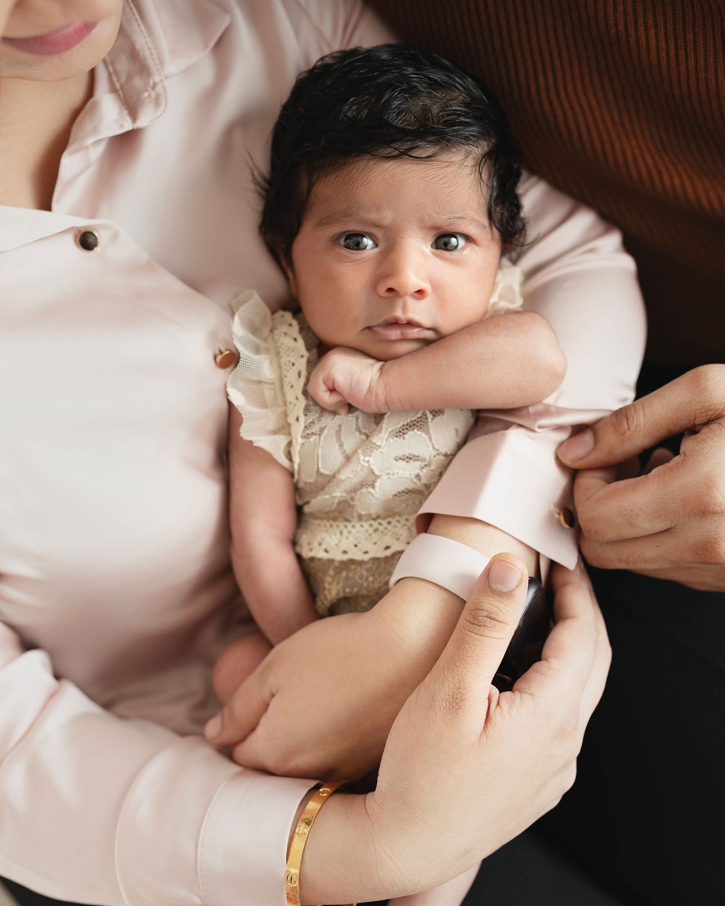 A series of intimate close-up photos showing gentle hands holding a small baby in delicate lace clothing.