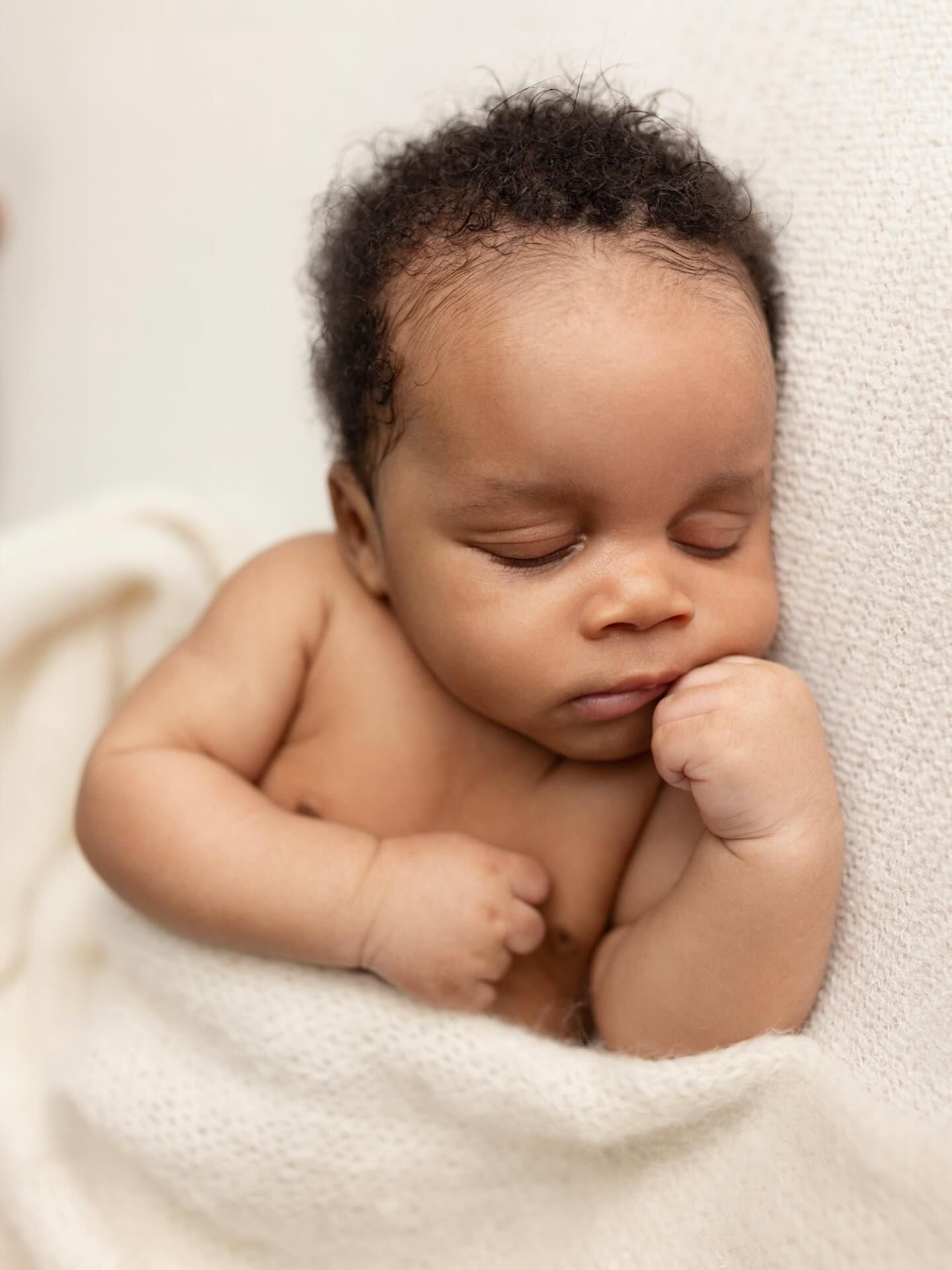 A peaceful sleeping newborn baby nestled in soft white textiles with natural lighting.