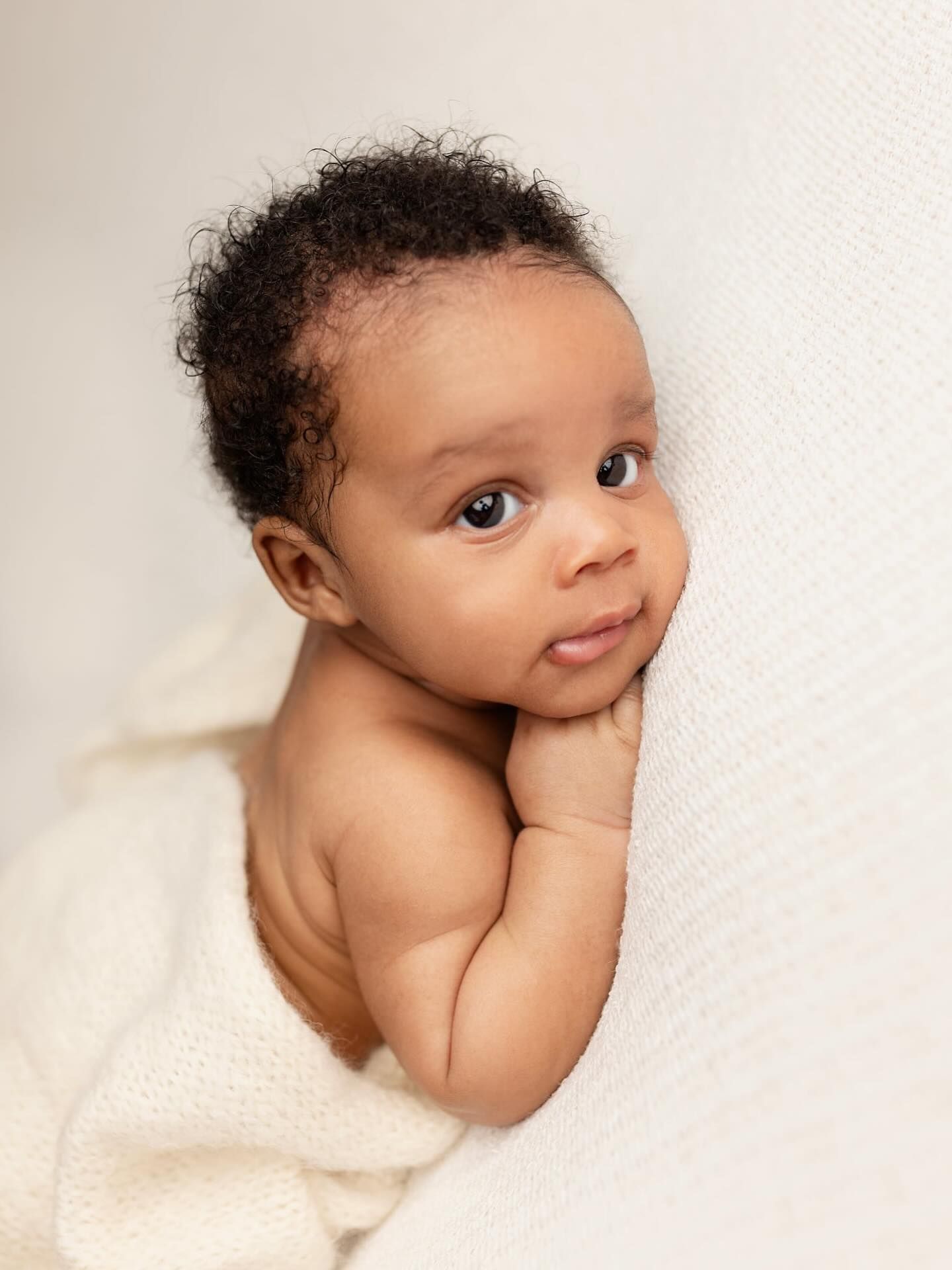 A sweet baby with curly hair peeks out from under a white blanket in a series of five artistic newborn portraits.
