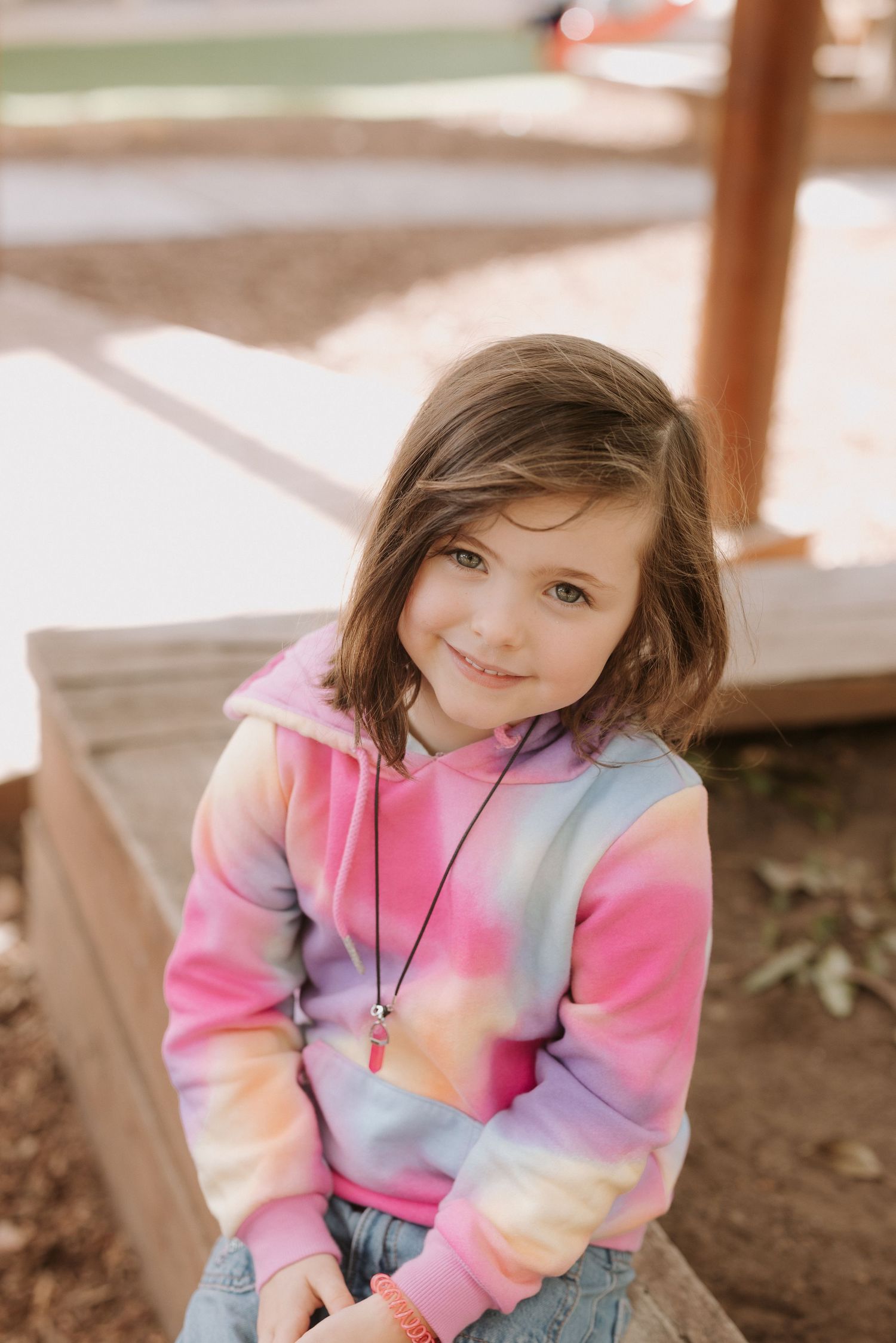 Child wearing navy and pink striped shirt with pigtails smiles while playing outdoors.