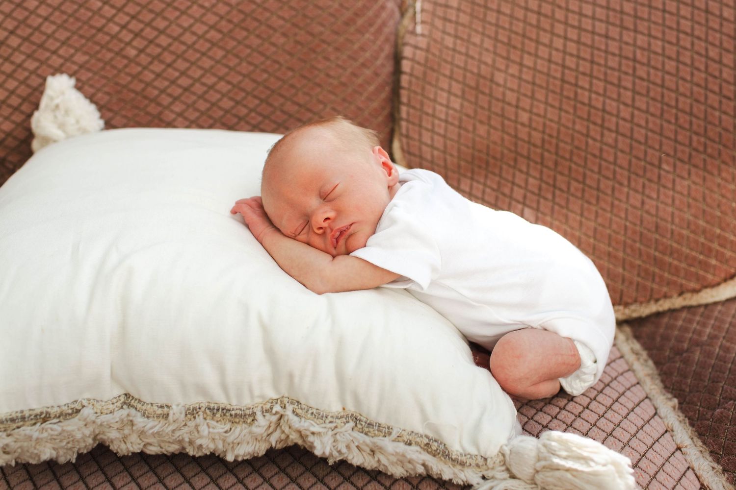 A newborn baby sleeps peacefully on white bedding while wearing a white outfit in a series of connected photos.