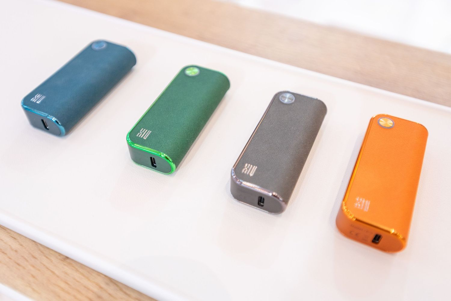 Colorful smartphone cases arranged in a row on a light wooden surface display various matte finishes and hues.