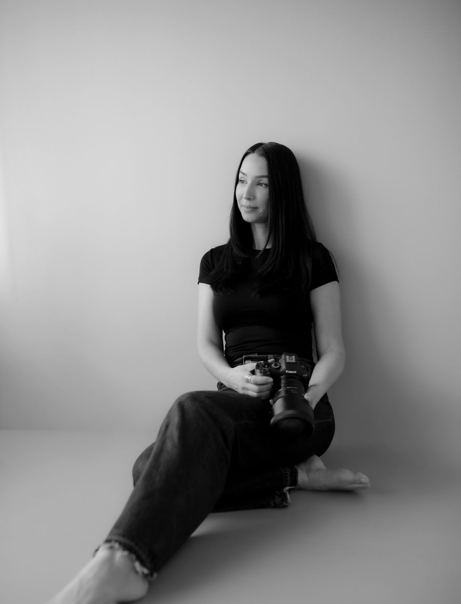 bild på Sabina som är fotograf. hon sitter lutad mot en vägg och håller i en kamera. bilden är i svartvitt.
