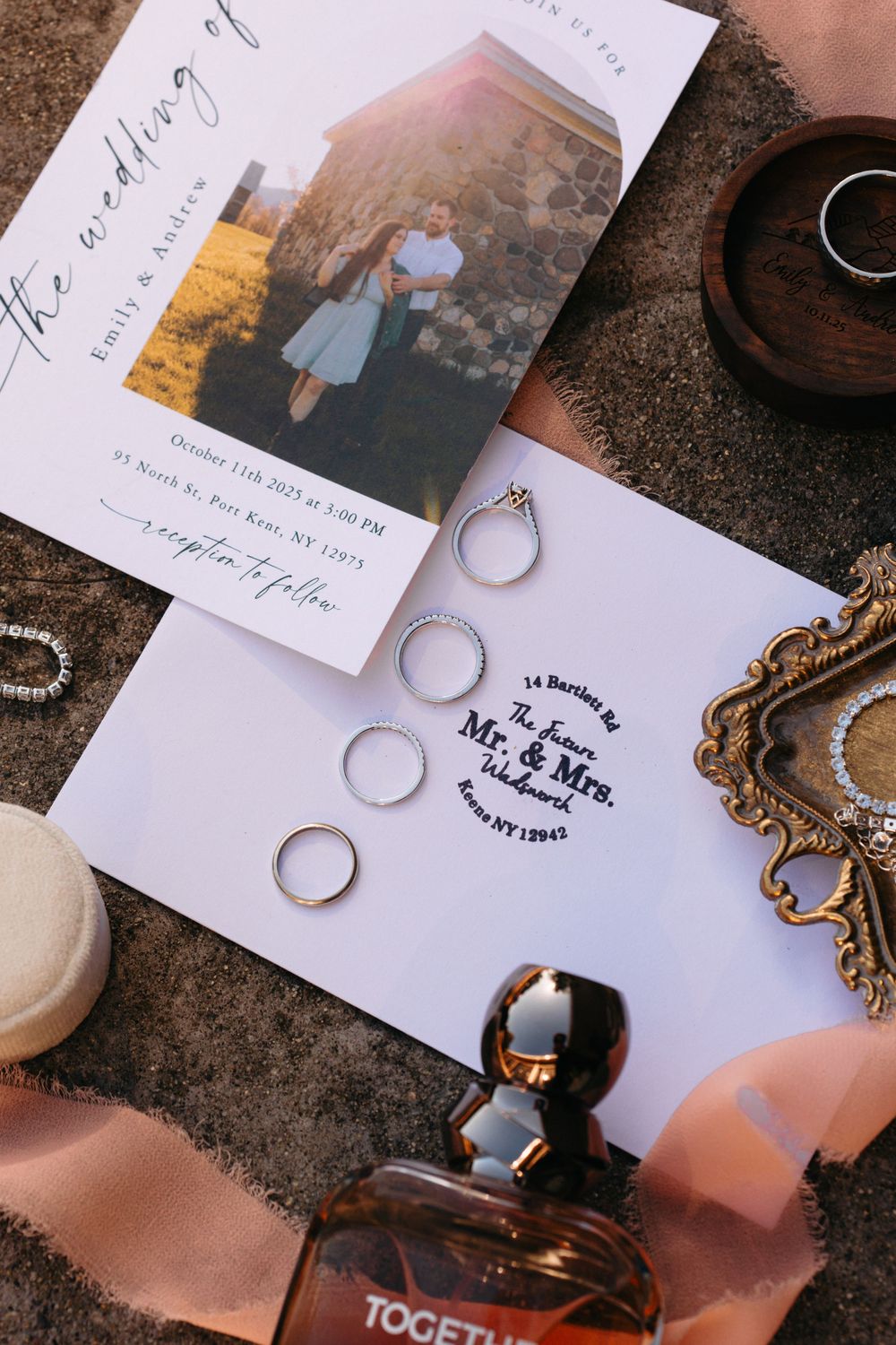 Wedding details flatlay featuring rings, perfume bottle, and engagement photo on white stationery.