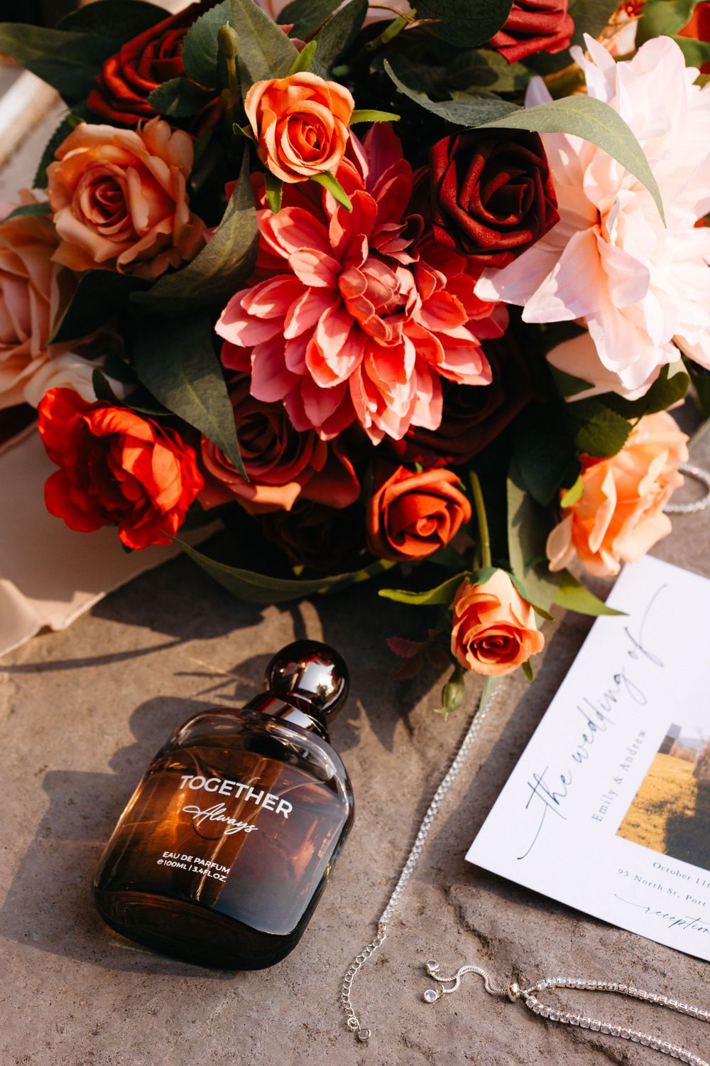 Perfume bottle surrounded by red and coral roses and a photograph on a concrete surface.