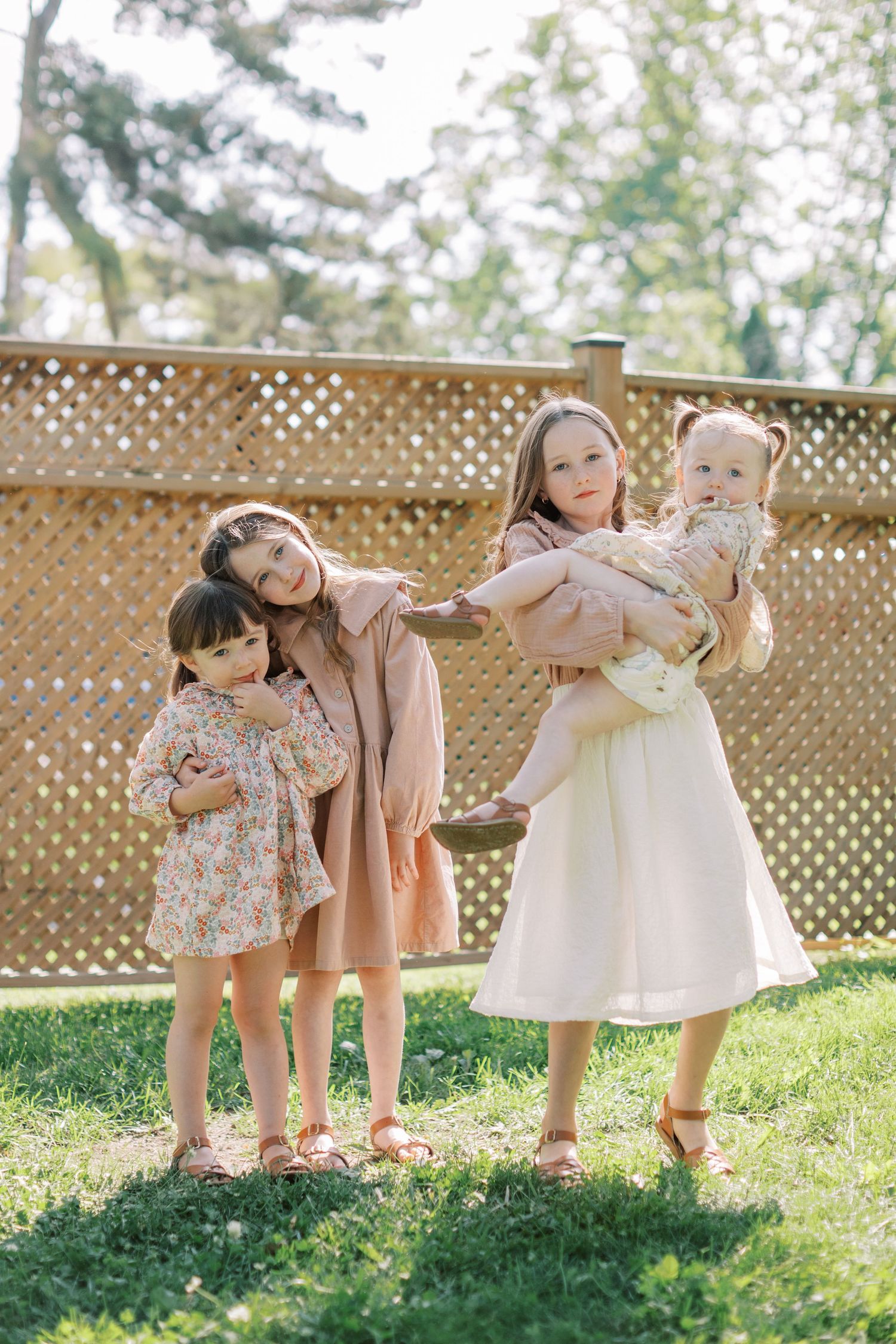 A series of four candid outdoor photos showing children playing and interacting on a grassy lawn with a lattice fence backdrop.