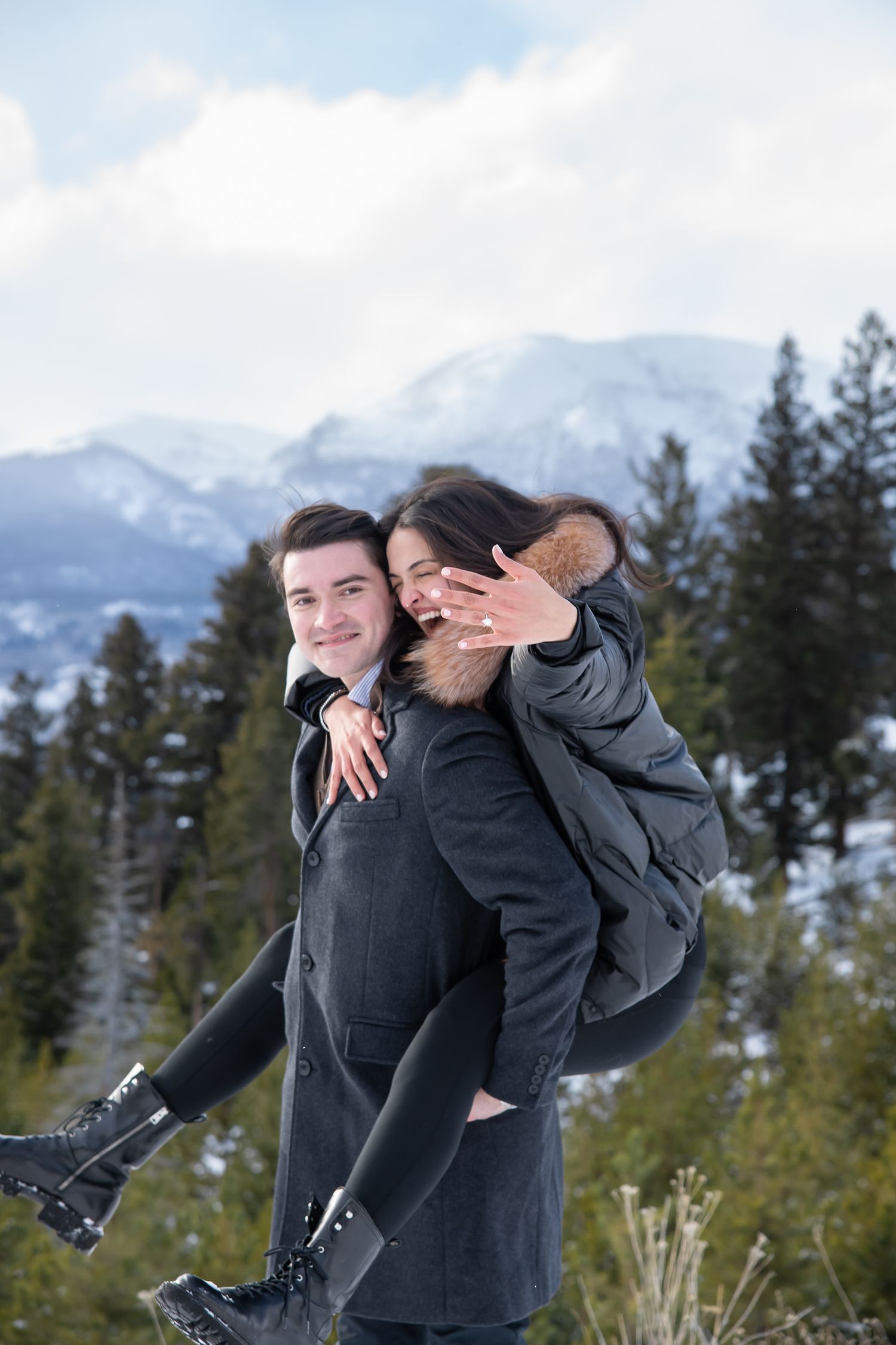 A playful piggyback ride against a scenic mountain backdrop with snow-capped peaks and evergreen trees after proposal at Sapphire Point.