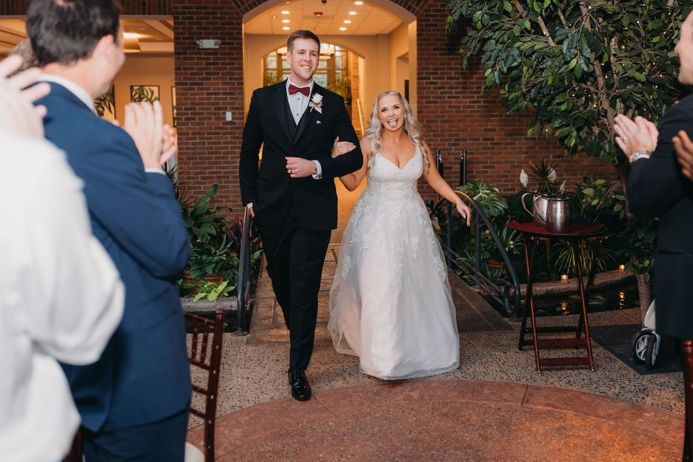 Wedding party dances and celebrates during evening reception at elegant brick venue with warm lighting.