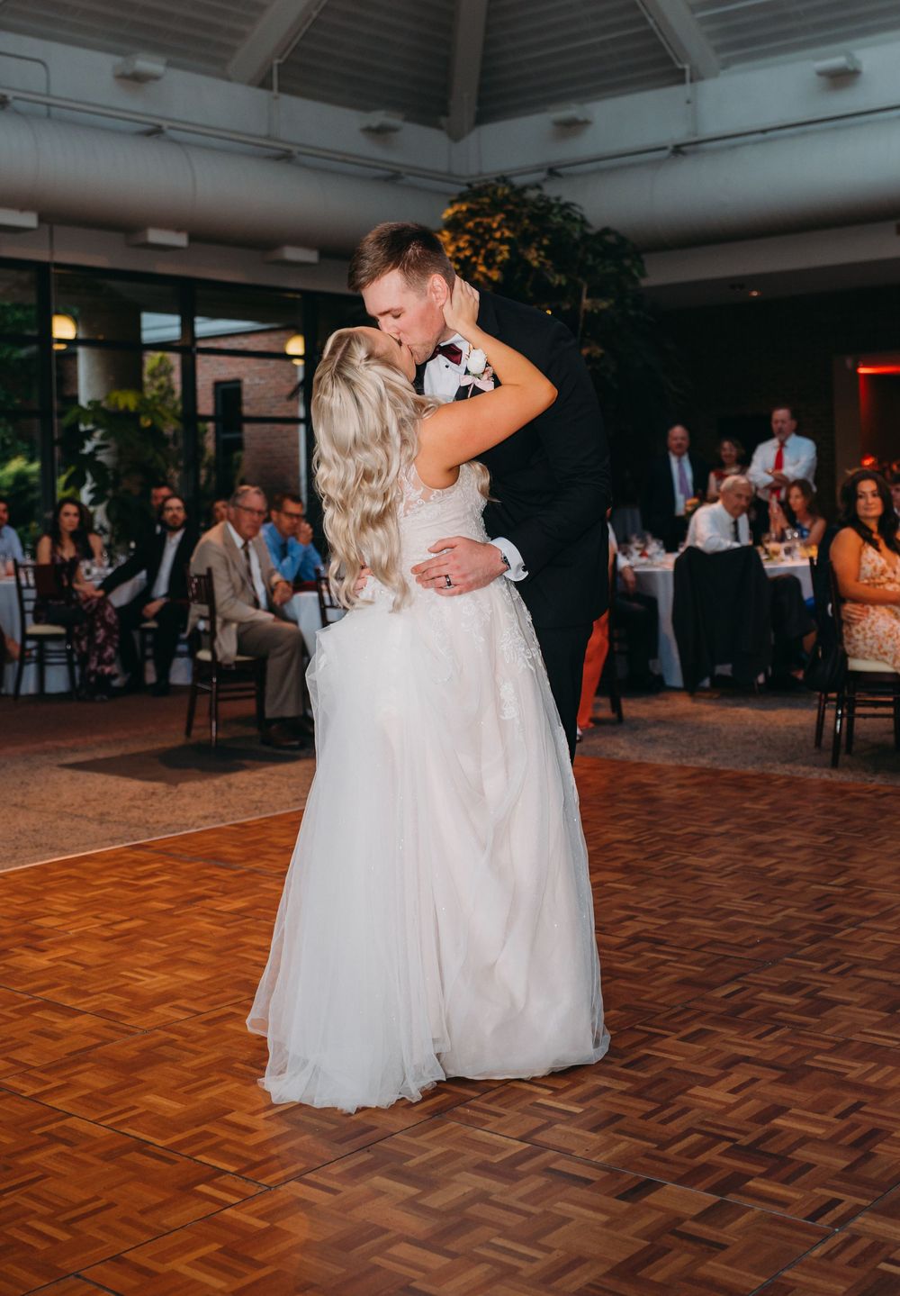 Wedding couple shares an intimate dance moment on a wooden dance floor surrounded by guests at their reception.