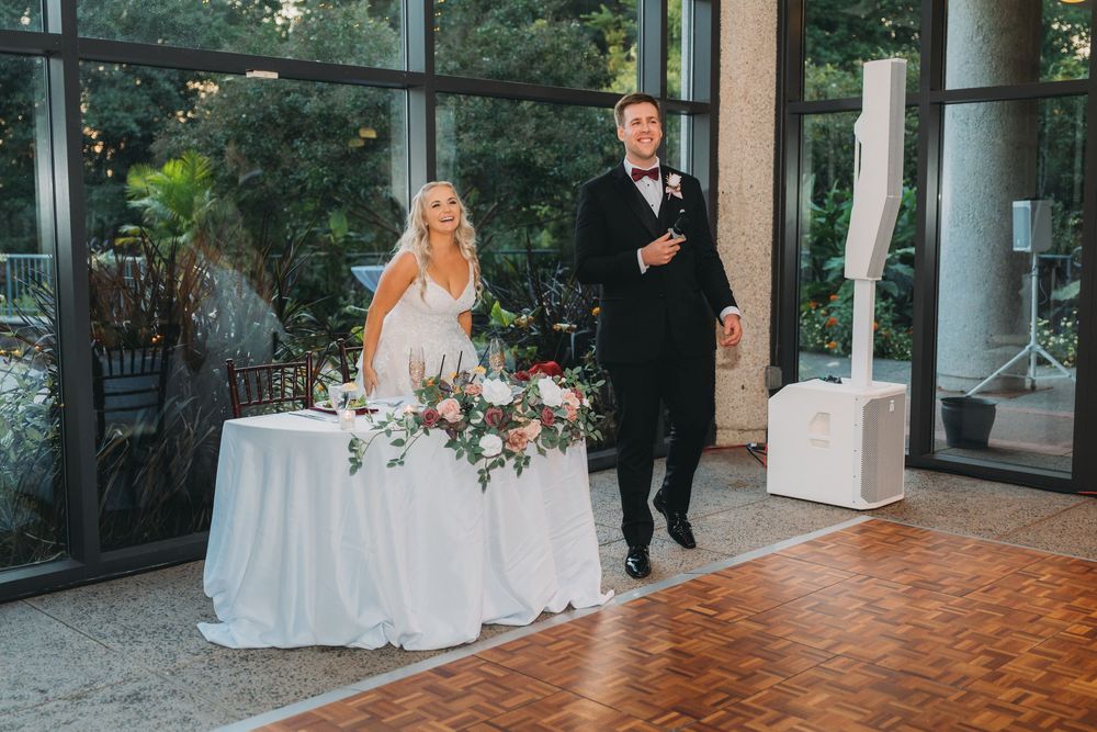 A couple poses together in formal wedding attire on a wooden dance floor during their reception celebration.