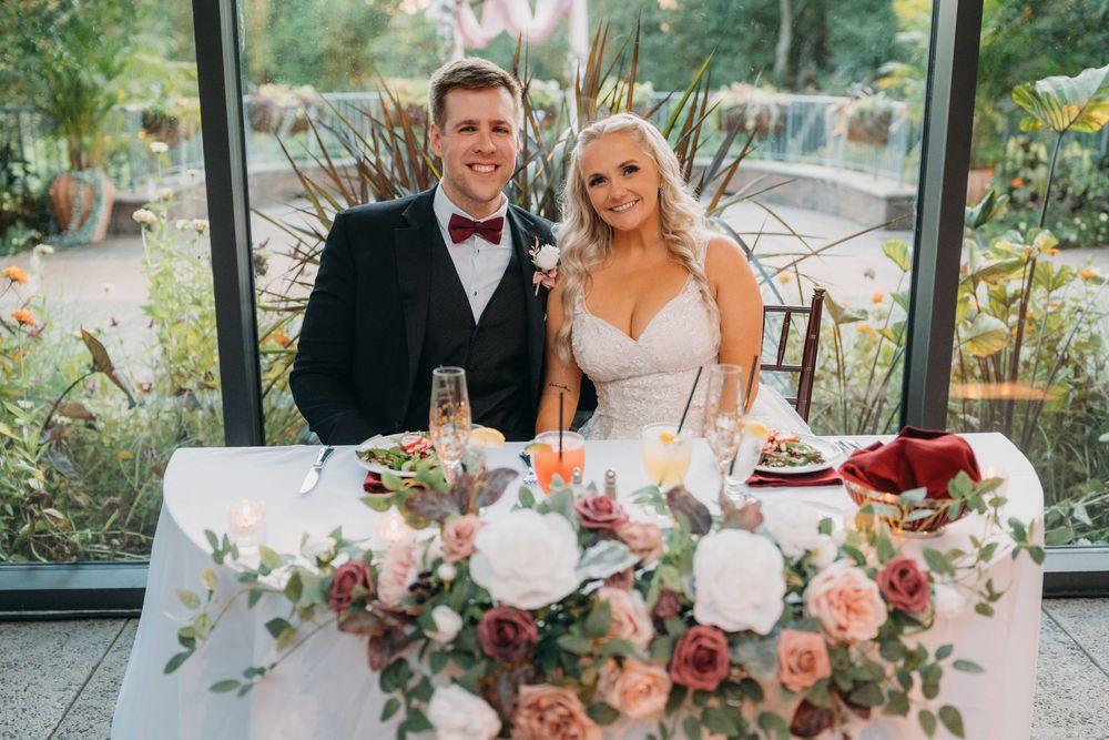 Elegant wedding reception table decorated with pink and white floral arrangements and candles in a garden setting.