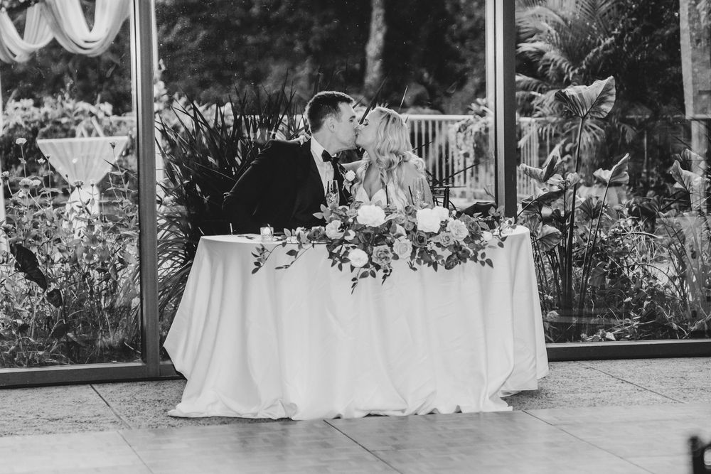 Wedding reception tables decorated with white linens and floral centerpieces set in an elegant outdoor garden venue.
