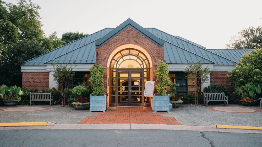 Panoramic exterior view of a brick building entrance with arched windows and covered walkway.
