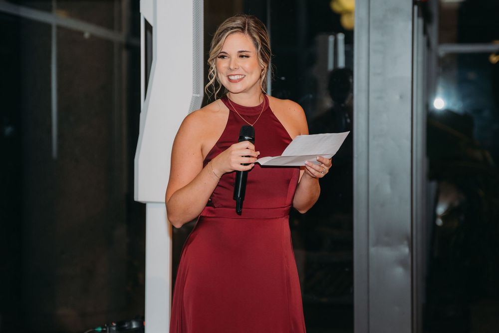 A person in a burgundy halter dress stands near glass doors in an indoor setting.