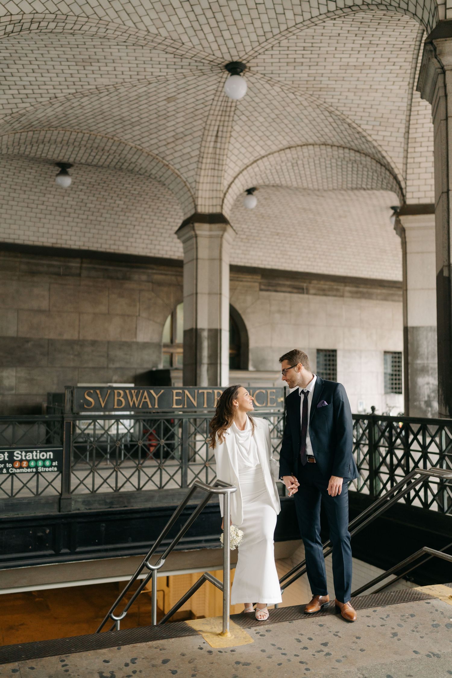 A couple stands together in an elegant vintage subway station with arched ceilings and classic architectural details.
