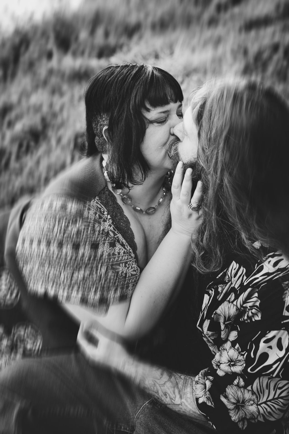 A tender black and white photograph of a couple sharing an intimate kiss outdoors.