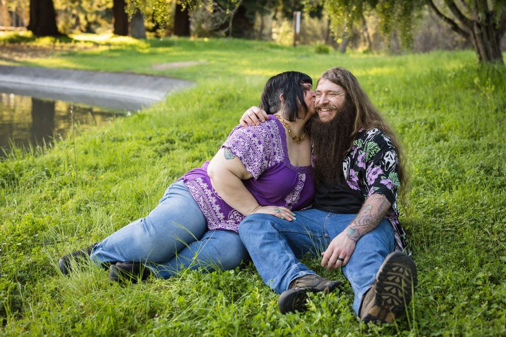 A couple relaxes together on a grassy hillside in a romantic outdoor setting during golden hour.