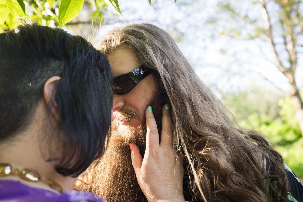 Two people share a tender moment outdoors on a sunny day with green foliage in the background.