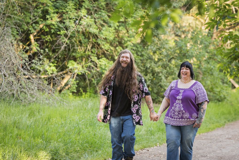 A couple walks hand in hand down a tree-lined path in a natural outdoor setting during autumn.