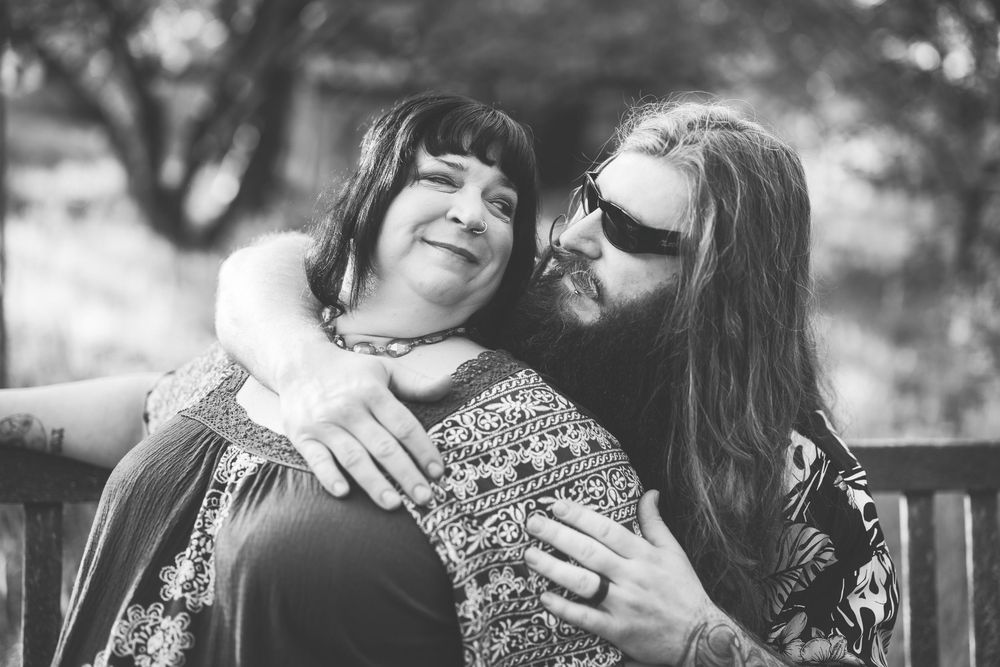 Black and white photo of two people sharing an intimate moment while sitting together on a bench outdoors.