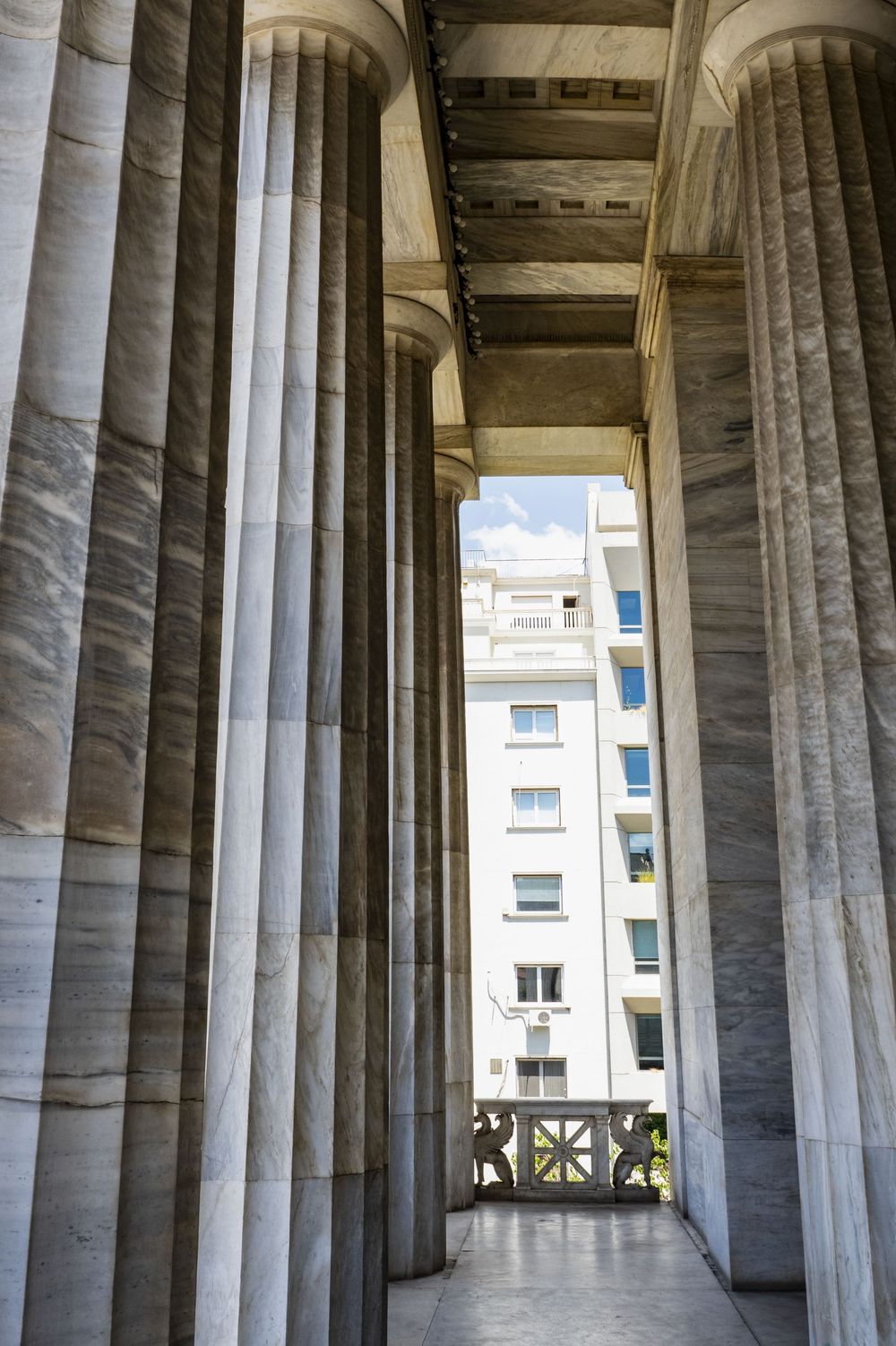 Architectural detail showing massive stone columns in a classical colonnade with modern buildings visible in background.