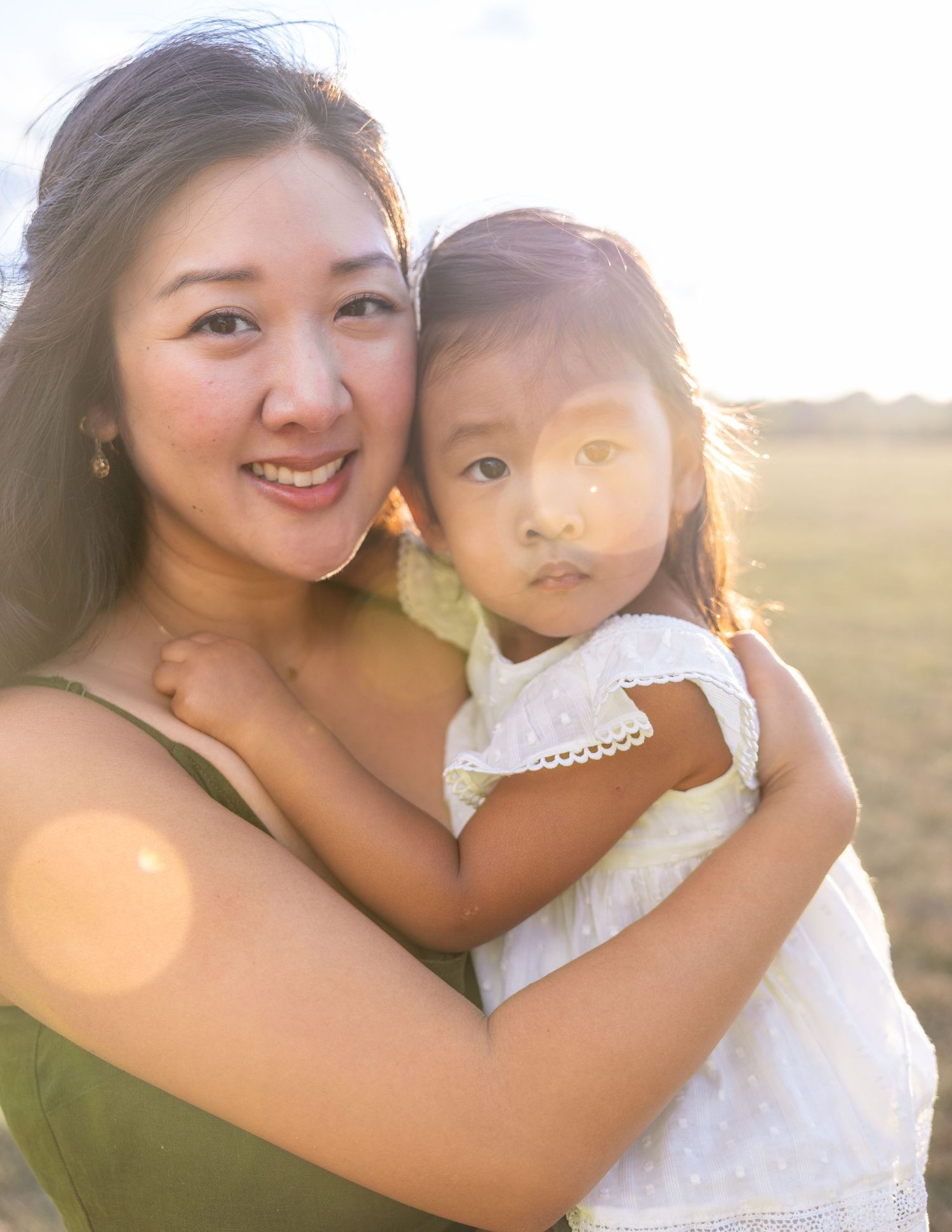 A tender moment captured between parent and child outdoors during golden hour with sunlight creating a warm glow.