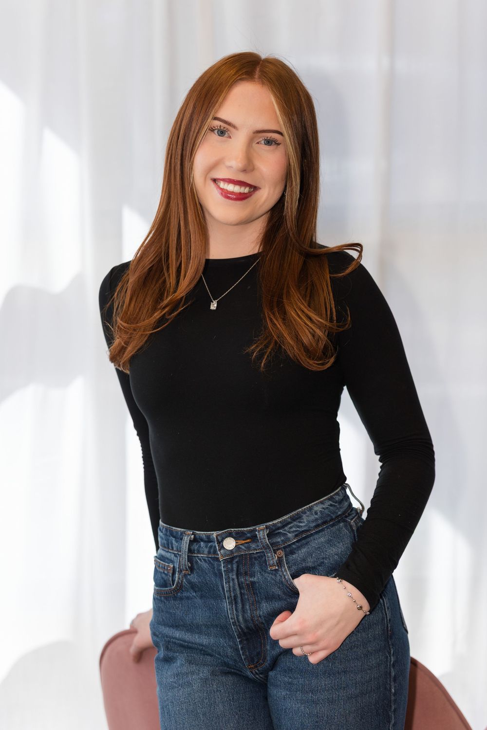 Lifestyle portrait of woman in black sweater and denim jeans against white backdrop.