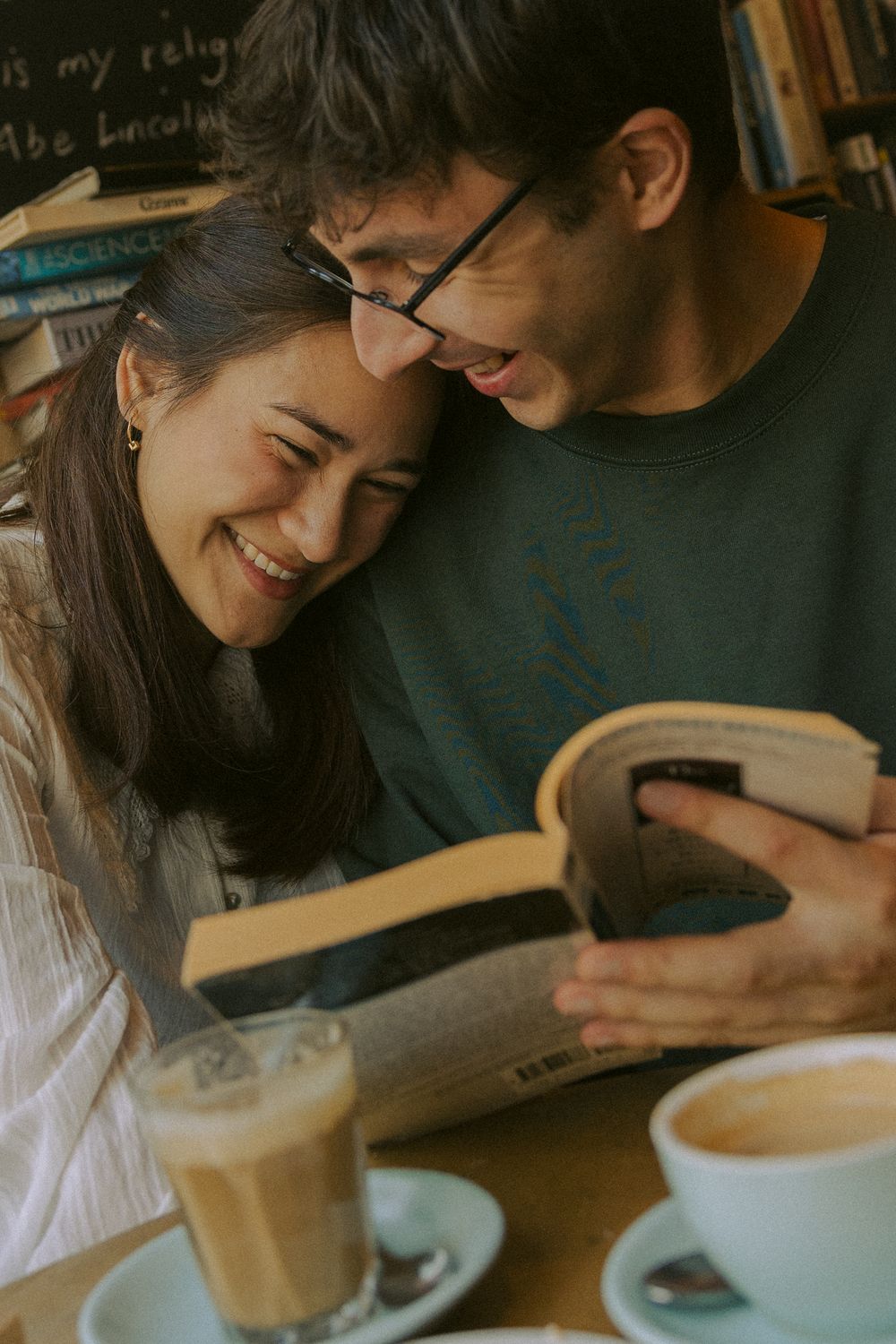 A couple enjoying coffee together at a cafe table while looking at something together with warm lighting.