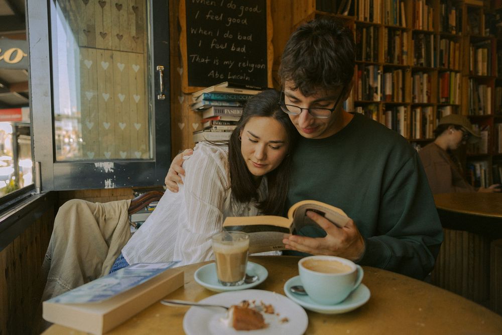 Students studying together at wooden tables in a library cafe surrounded by bookshelves.