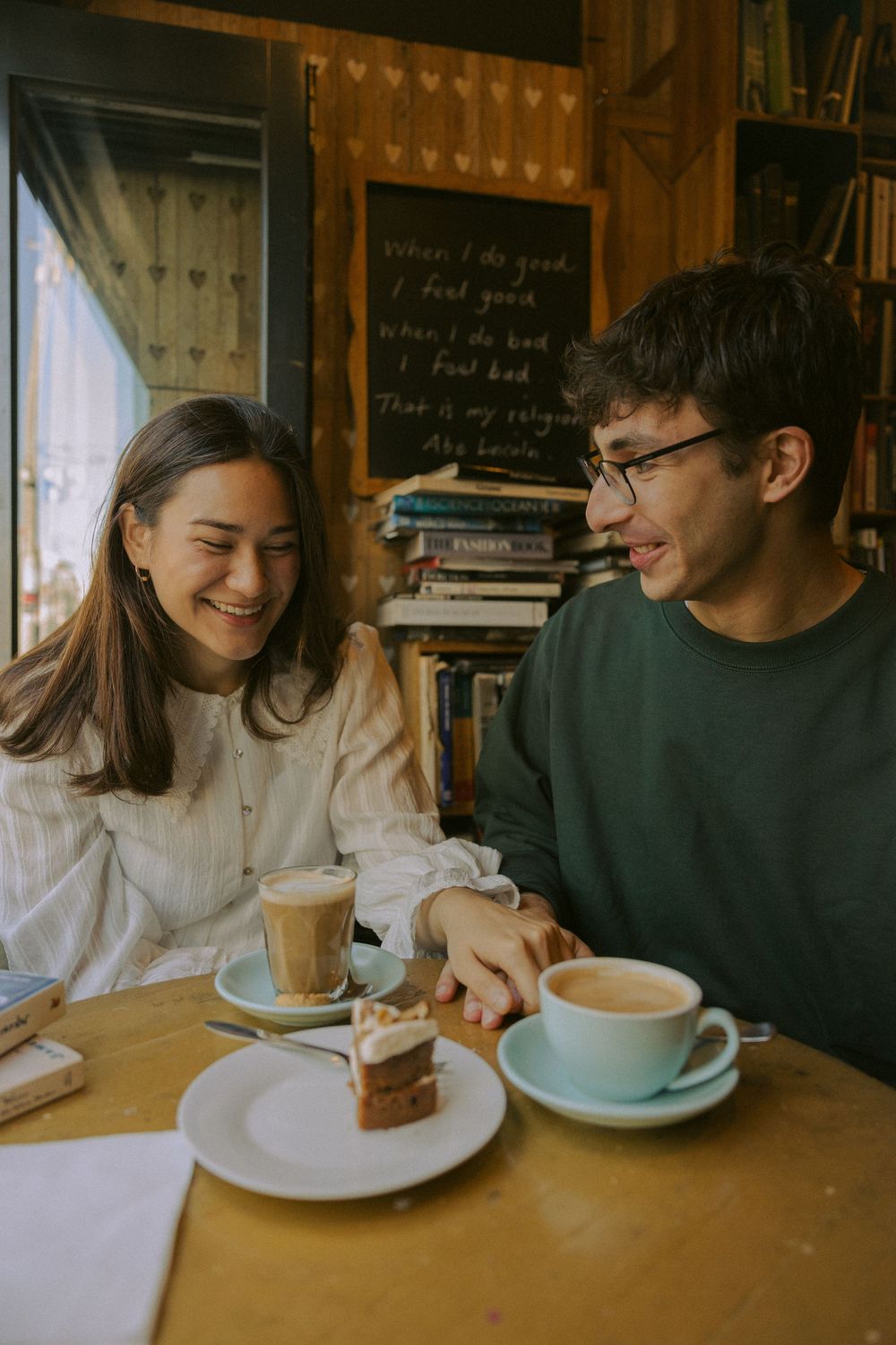 Couple enjoying coffee and dessert at a cozy cafe with bookshelves in the background.