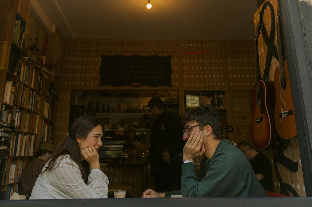 Two people sit across from each other in a cozy room filled with bookshelves and warm lighting.