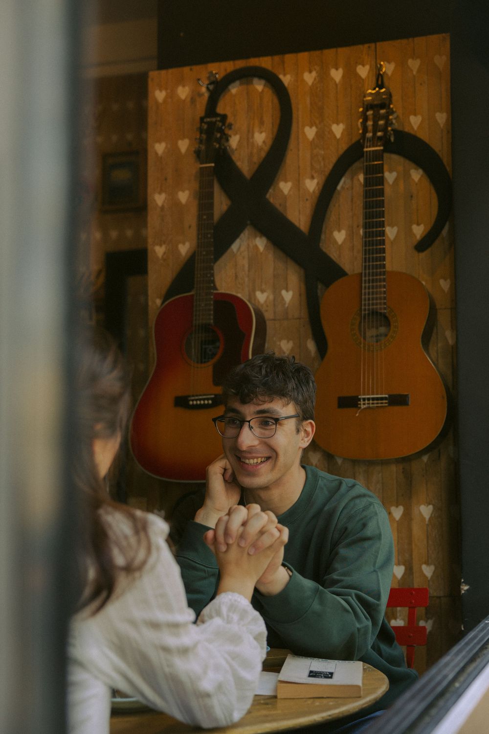A romantic coffee date scene with acoustic guitars mounted on a heart-patterned wall in the background.