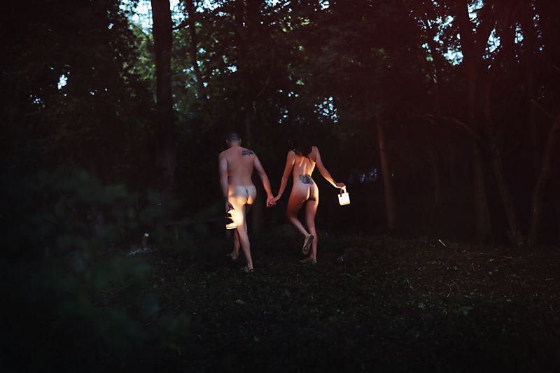 People walking through a dark forest lit by moonlight and lanterns.