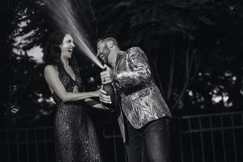 Black and white image showing two people joyfully spraying champagne outdoors during a celebration.