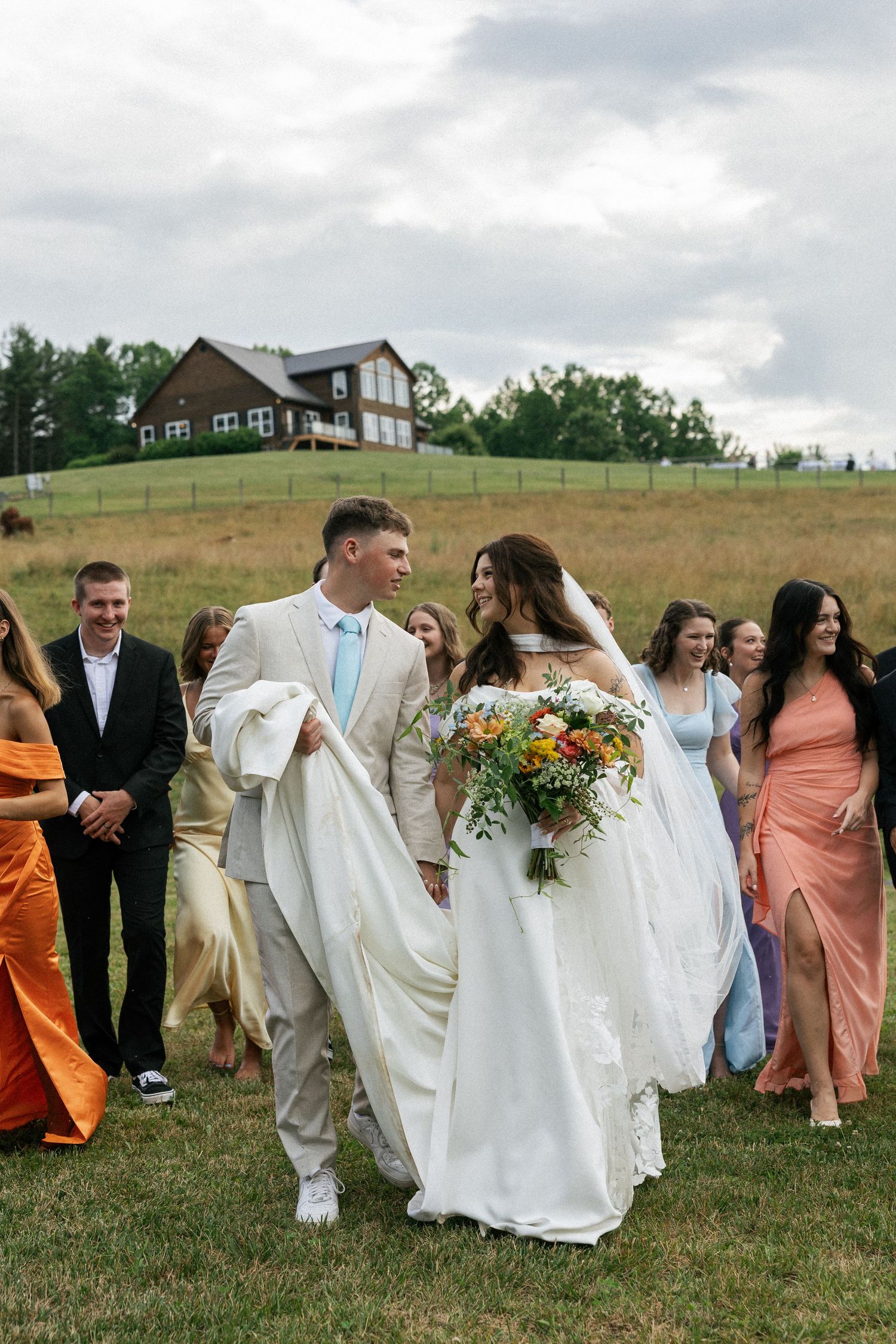 Wedding party walking through grassy field in formal attire and flowing dresses.Micro wedding, elopement, intentional celebration