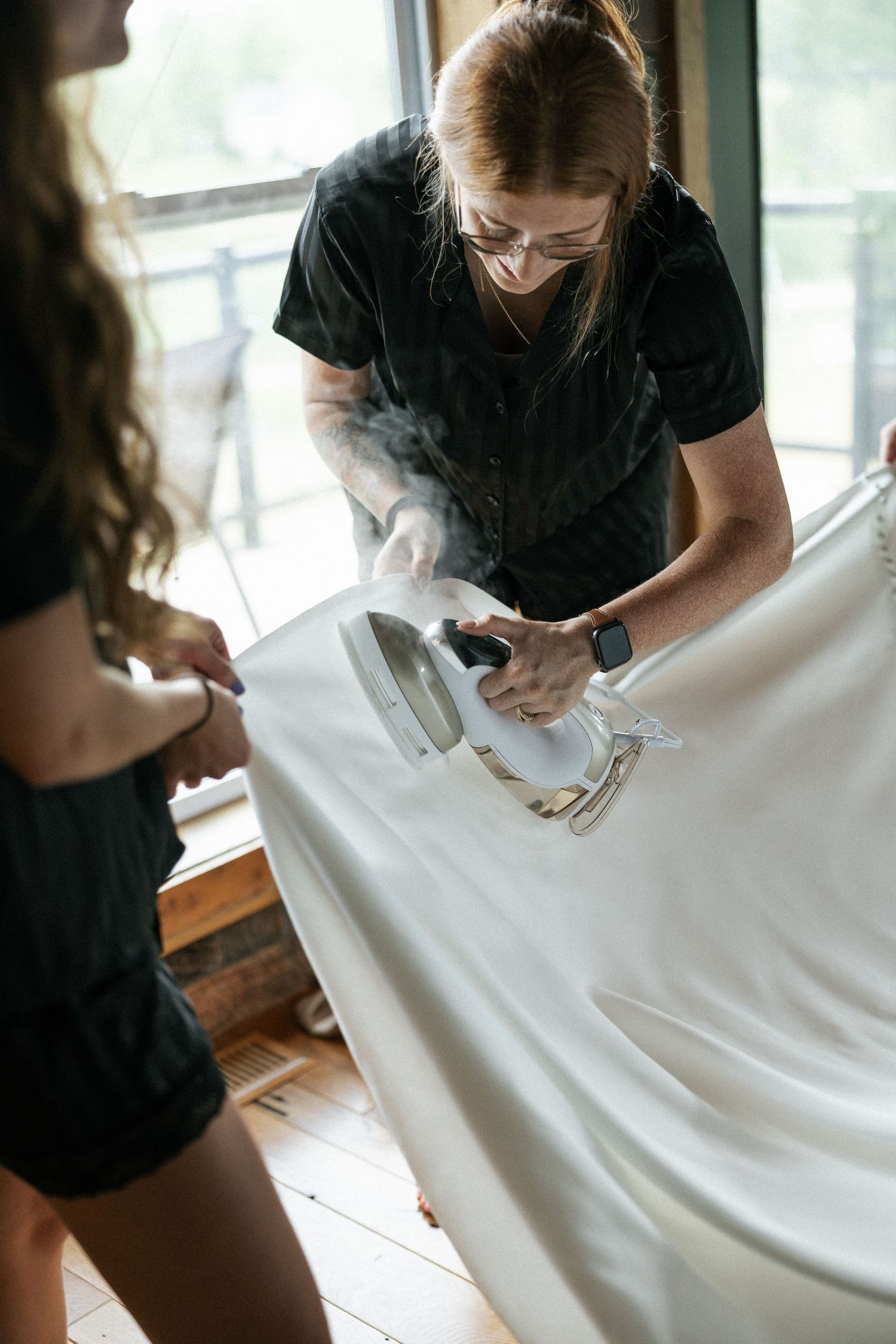 Someone carefully working on intricate details of a white wedding dress on a table.Micro wedding, elopement, intentional celebration
