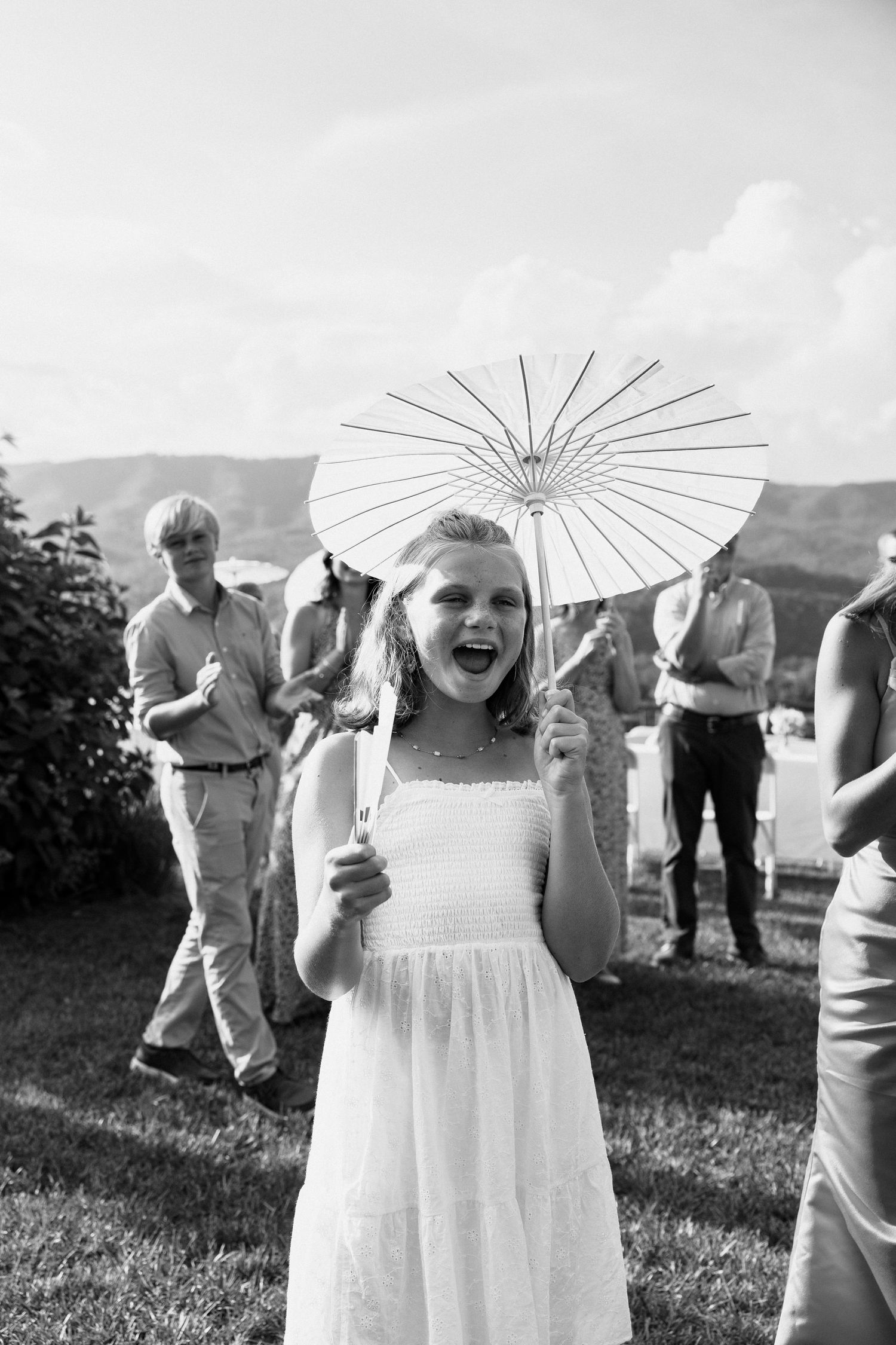 A series of black and white photos showing a young attendant in a white dress holding a parasol at an outdoor event.